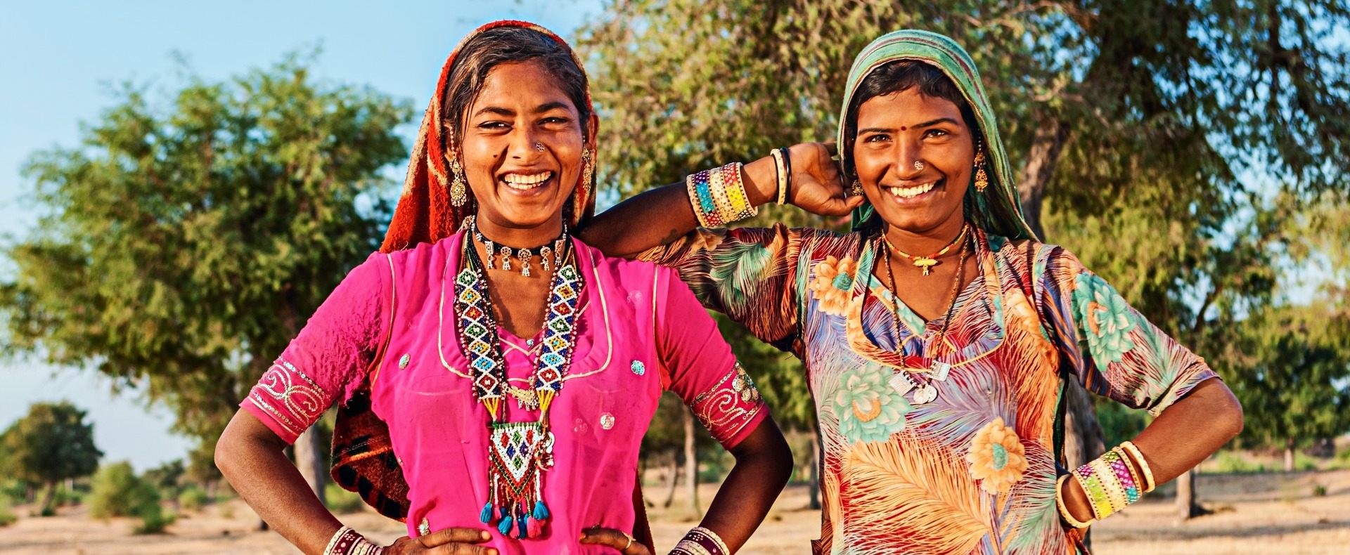 Two Indian women smiling at the camera with colorful dresses
