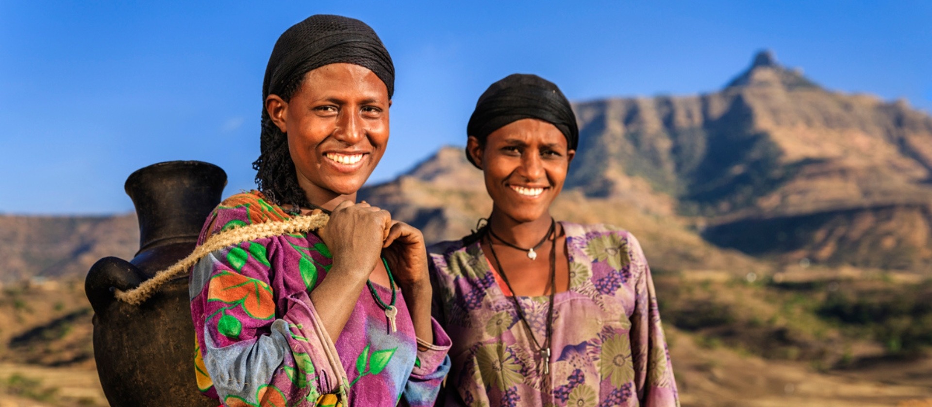 Two women smiling at the camera with mountains in the background