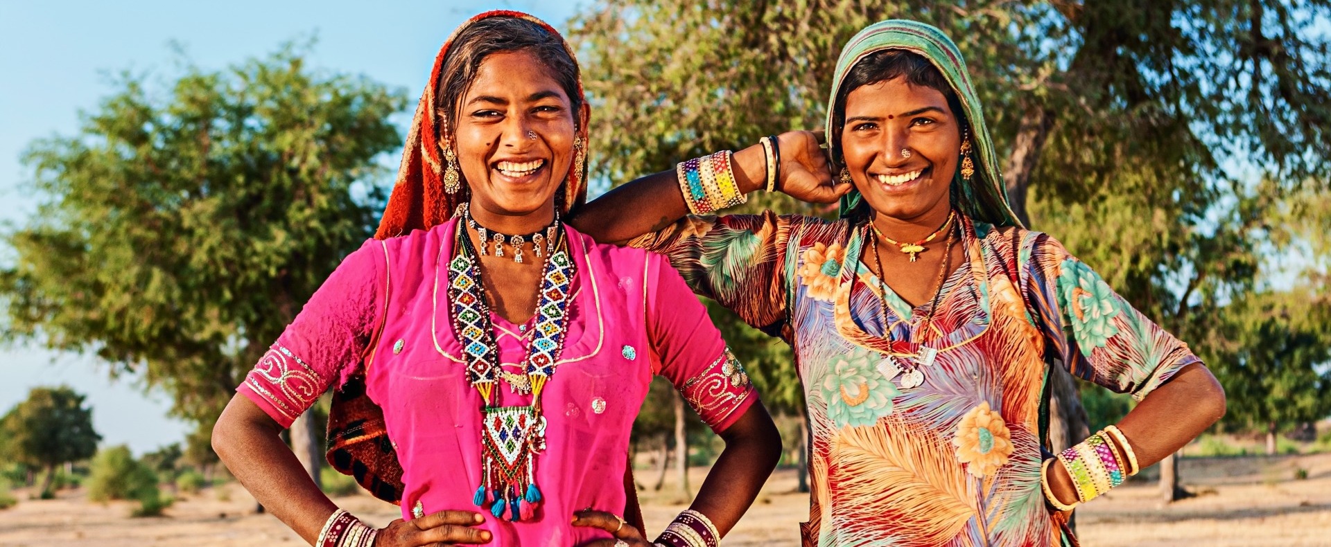 Two Indian women smiling at the camera with colorful dresses