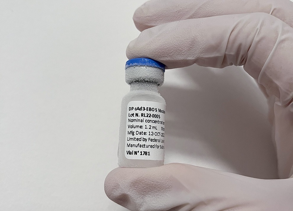A gloved hand holds a vaccine vial.