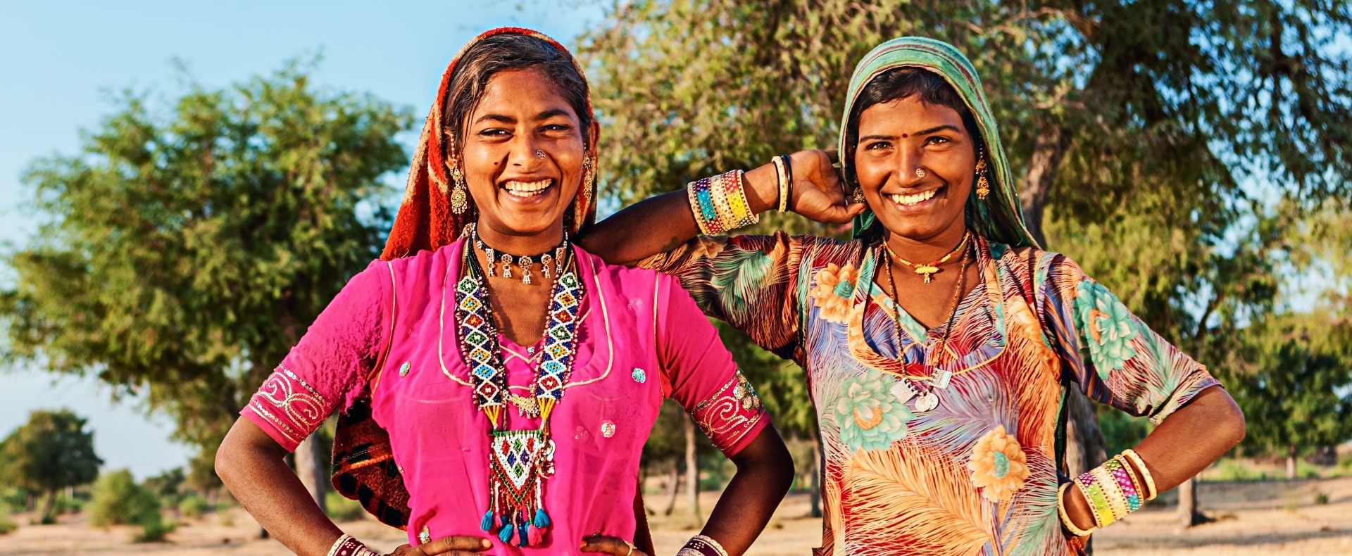 Two Indian women smiling at the camera with colorful dresses